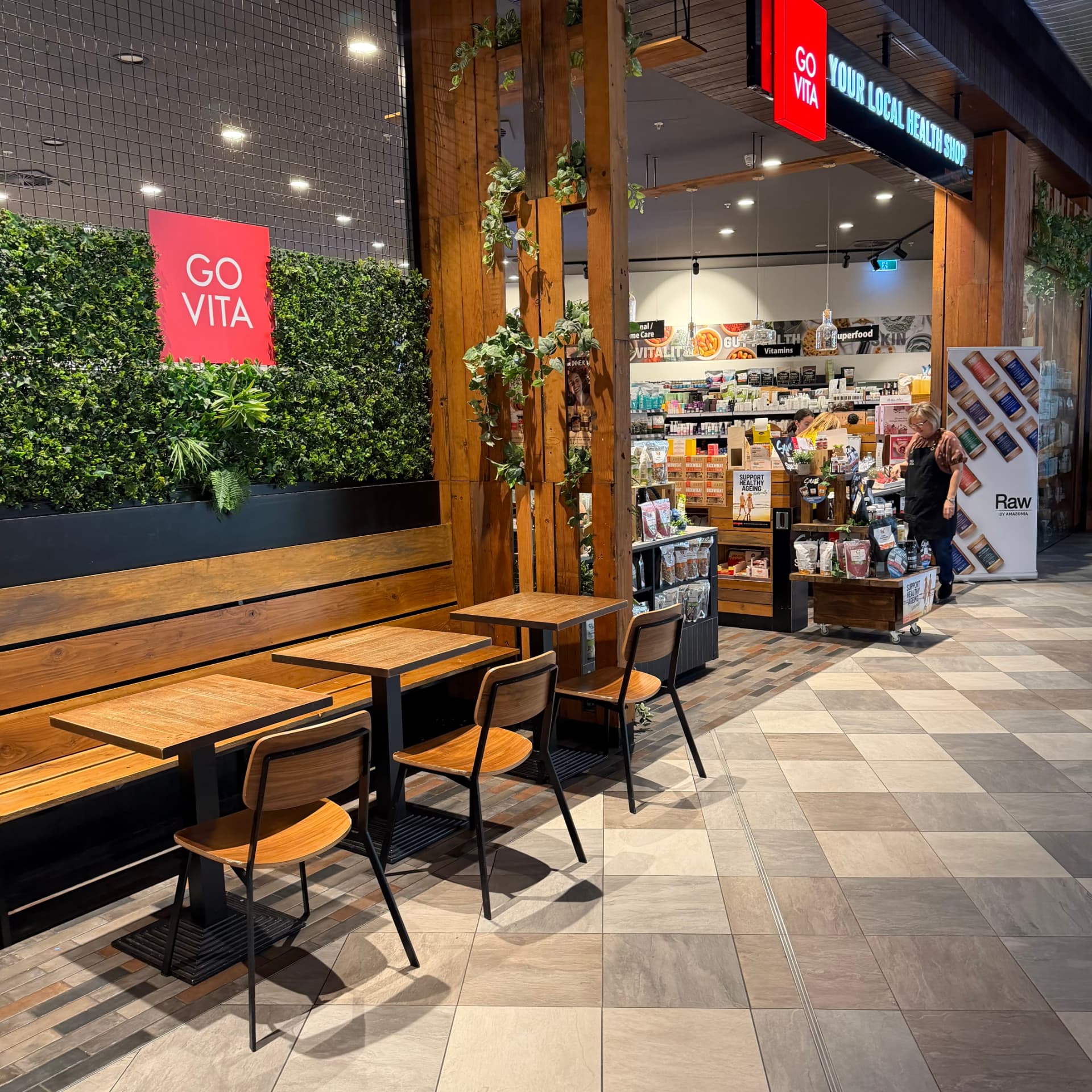 Outdoor café seating area with wooden benches and greenery at Go Vita Midland